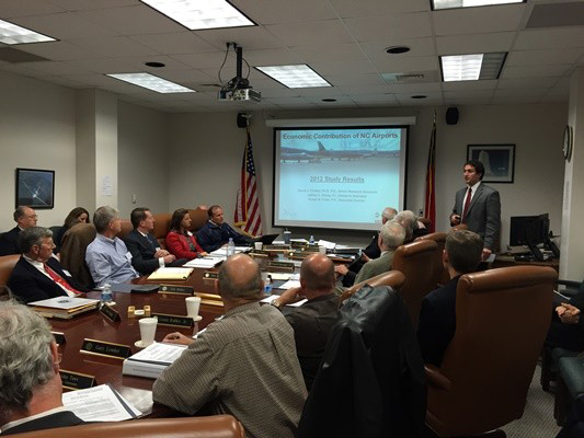 Aviation Task force seated at long table, watching a 2014 airports presentation by Daniel Findley