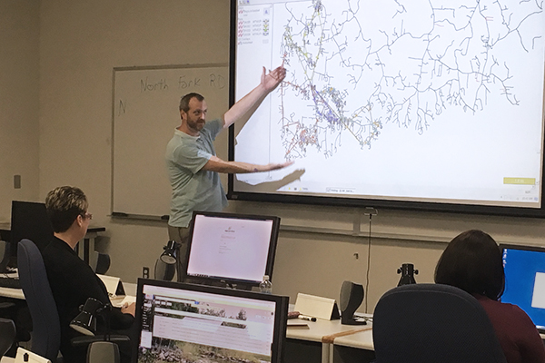 Kevin Hart gesturing to a large screen projection of a map diagram for a TIMS class