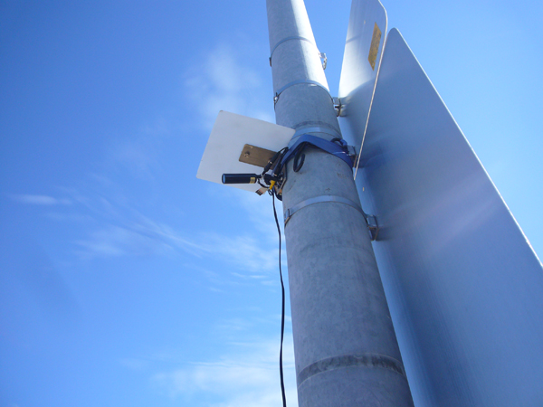 Sensor attached to a thick metal roadside pole, framed against the sky