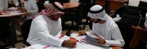 two men wearing Ghutrah style head scarves place orange markers on a diagram of a road while consulting instructional roadway materials