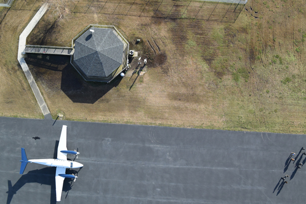 Top-down view of small plane on a landing strip with visible airport command tower