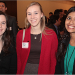 Three smiling women at a conference, with other business professionals in the background