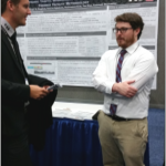 Two men in suits stand in front of an ITRE research poster