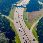 Aerial view of a highway with light traffic. Dense trees dominate the adjacent landscape.