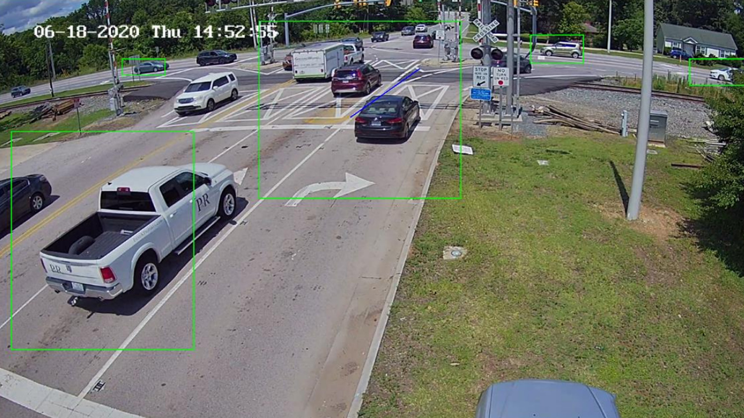 Several vehicles traverse a rail crossing, with green boxes overlaid by computer software