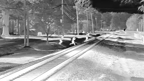 Thermal camera view of three people running across a railroad track