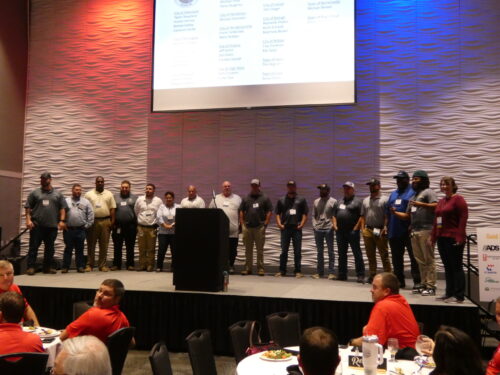 15 graduates and the Director of NCLTAP standing on a stage receiving applause for graduating basic Roads Scholar program.