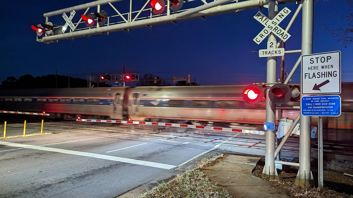 Amtrak train transiting a grade crossing at night, with the crossing signal lights flashing and barriers lowered.